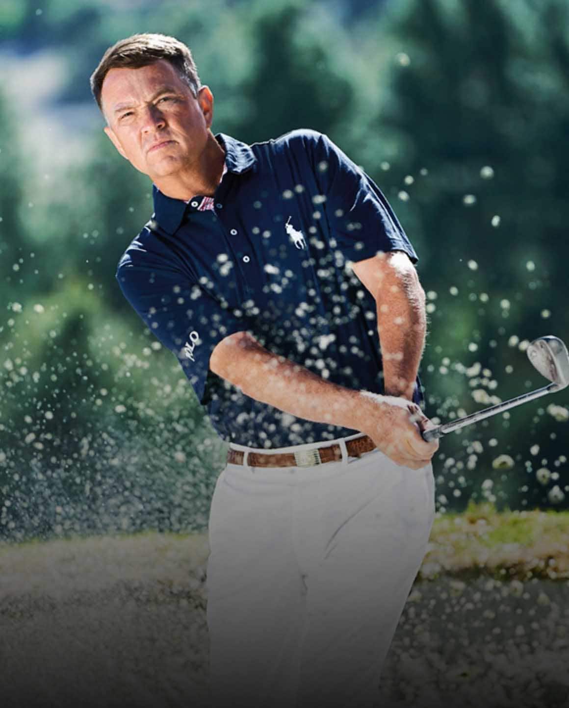 Photo of Davis Love III swinging golf club in navy Polo and white pants.