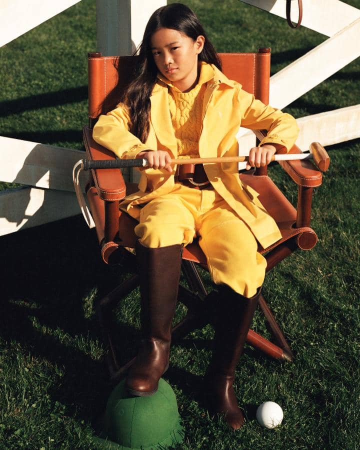Girl in brown leather director’s chair wears yellow outfit and riding boots.